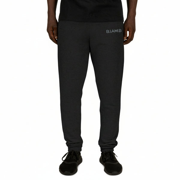 Front view of a person wearing black B.I.AM.B joggers with a small logo on the left thigh, styled with a black shirt and black sneakers on a plain background.