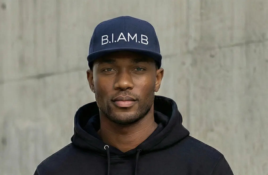 Model wearing B.I.AM.B navy snapback hat with black hoodie lifestyle portrait streetwear Because I Am Black brand
